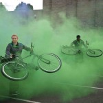 Performers swing their bikes around amidst a cloud of green smoke