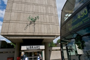 Two green bicycles emerge from the wall above Roehampton Library