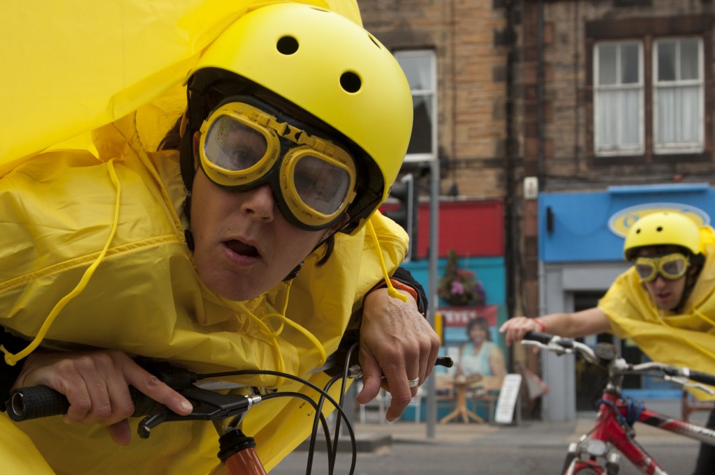 Kate Evans, wearing a yellow helmet, goggles & rain cape, stares into the camera